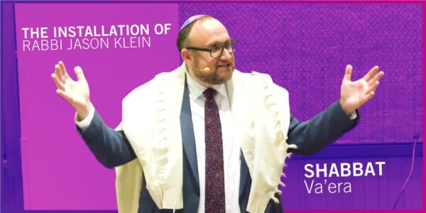 Rabbi Jason Klein gestures in the pulpit, and behind him reads - Installation Shabbat - Shabbat Va'era